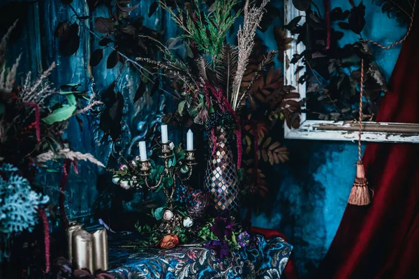 Kurumuş çiçekler, vazolar, avizeler, altın çerçeveli kumaşlar, lüks kraliyet tarzı ahşap bir masa, eski fenerlerle yanan mumlar.