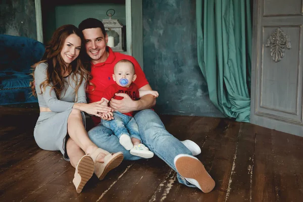 Mutlu ebeveynler, erkek bebekle odada poz veriyorlar.