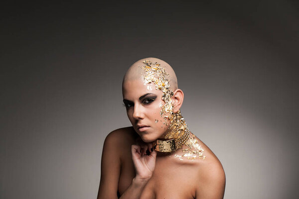 Portrait of bold and naked woman with gold elements