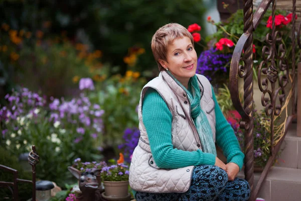 Adult woman retired gardener in her blooming garden on the background of the house