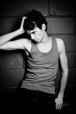 Gri tişörtlü, esmer, genç bir adam beton duvara karşı poz veriyor.