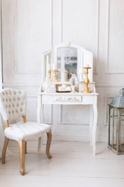 Güzel, beyaz bir iç mekan. Ahşap zemin aydınlatma duvarlı klasik oda pervazlı sandalye aynalı tuvalet masası, altın elementlerle süslenmiş.