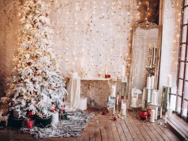 Sıcak bir akşam konforlu Noel odası iç tasarımı, altın ışıklarla süslenmiş Xmas ağacı hediyeler, mumlar, ayna şeklinde aydınlatma şöminesi. Tatil salonu. Yeni yıl tatili konsepti