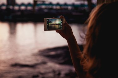 Kadın şehirde cep telefonunun fotoğrafını çekiyor.