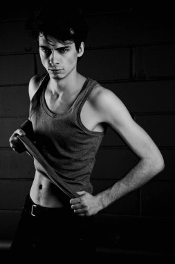 Gri tişörtlü, esmer, genç bir adam beton duvara karşı poz veriyor.