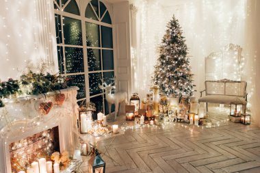 Noel iç tasarımında sıcak ve sıcak bir akşam, ışıklarla süslenmiş Xmas ağacı hediyeler, oyuncaklar, geyikler, mumlar, fenerler, kapalı alanda yanan çelenkler.