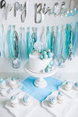 Bir yaşındaki erkek bebeğin onuruna şenlikli bir dekor. Kürsüde beyaz pasta, kekler, mavi toplar ve süslemeler. 