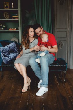 Mutlu ebeveynler stüdyodaki kanepede oğluyla poz veriyor.