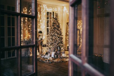 Noel iç tasarımında sıcak ve sıcak bir akşam, ışıklarla süslenmiş Xmas ağacı hediyeler, oyuncaklar, geyikler, mumlar, fenerler, kapalı alanda yanan çelenkler.