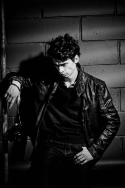 Duvarın yanında duran deri ceketli yakışıklı manken.