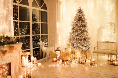Noel iç tasarımında sıcak ve sıcak bir akşam, ışıklarla süslenmiş Xmas ağacı hediyeler, oyuncaklar, geyikler, mumlar, fenerler, kapalı alanda yanan şömine. tatil salonu sihirli yeni yıl