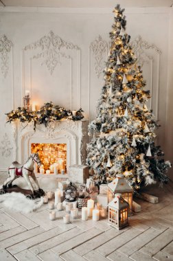Beyaz bir odanın içinde Noel ağacı, süslü bir şömine, sallanan at ve yeni yıl hediyeleri olan bir oda.
