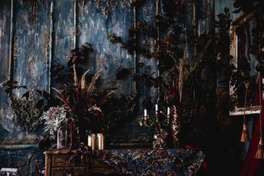 Kurumuş çiçekler, vazolar, avizeler, altın çerçeveli kumaşlar, lüks kraliyet tarzı ahşap bir masa, eski fenerlerle yanan mumlar.