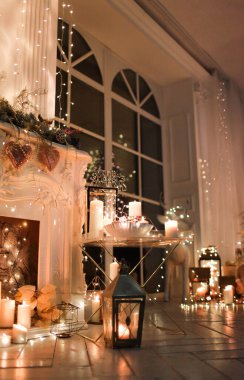 Noel iç tasarımında sıcak ve sıcak bir akşam, ışıklarla süslenmiş Xmas ağacı hediyeler, oyuncaklar, geyikler, mumlar, fenerler, kapalı alanda yanan şömine. tatil salonu sihirli yeni yıl