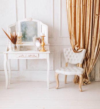 Güzel, beyaz bir iç mekan. Ahşap zemin aydınlatma duvarlı klasik oda pervazlı sandalye aynalı tuvalet masası, altın elementlerle süslenmiş.