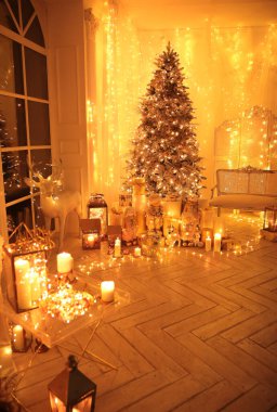 Noel iç tasarımında sıcak ve sıcak bir akşam, ışıklarla süslenmiş Xmas ağacı hediyeler, oyuncaklar, geyikler, mumlar, fenerler, kapalı alanda yanan çelenkler.