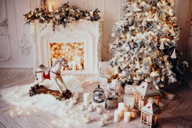 Beyaz bir odanın içinde Noel ağacı, süslü bir şömine, sallanan at ve yeni yıl hediyeleri olan bir oda.