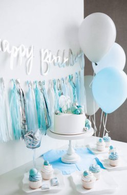 Bir yaşındaki erkek bebeğin onuruna şenlikli bir dekor. Kürsüde beyaz pasta, kekler, mavi toplar ve süslemeler. 