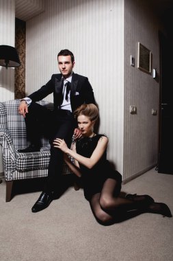 Odadaki gölgelerde klasik giysiler içinde tutkulu güzel bir çift: sandalyede oturan adam, ayaklarının dibinde yatan kadın.