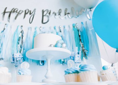 Bir yaşındaki erkek bebeğin onuruna şenlikli bir dekor. Kürsüde beyaz pasta, kekler, mavi toplar ve süslemeler. 