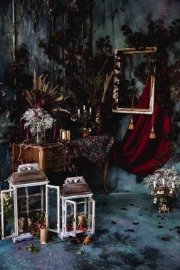 Kurumuş çiçekler, vazolar, avizeler, altın çerçeveli kumaşlar, lüks kraliyet tarzı ahşap bir masa, eski fenerlerle yanan mumlar.