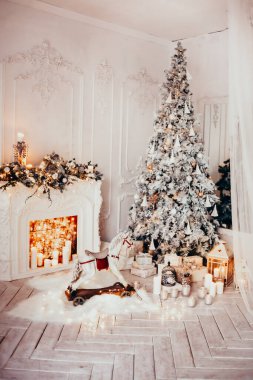 Beyaz bir odanın içinde Noel ağacı, süslü bir şömine, sallanan at ve yeni yıl hediyeleri olan bir oda.
