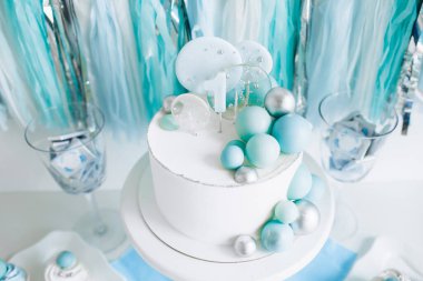 Bir yaşındaki erkek bebeğin onuruna şenlikli bir dekor. Kürsüde beyaz pasta, kekler, mavi toplar ve süslemeler. 