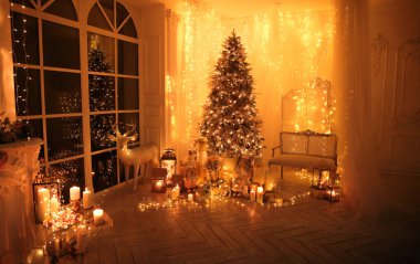 Noel iç tasarımında sıcak ve sıcak bir akşam, ışıklarla süslenmiş Xmas ağacı hediyeler, oyuncaklar, geyikler, mumlar, fenerler, kapalı alanda yanan çelenkler.