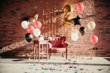 Çocuk doğum günü şerefine 2 yıl, stüdyo dairede, güneş ışığıyla dolu. Klasik turuncu sandalye, pasta masası, kırmızı, siyah, altın balonlar tuğla duvar zemininde