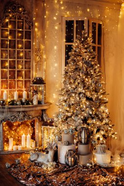 Noel iç tasarımında sıcak ve sıcak bir akşam, ışıklarla süslenmiş Xmas ağacı hediyeler, oyuncaklar, geyikler, mumlar, fenerler, kapalı alanda yanan çelenkler.