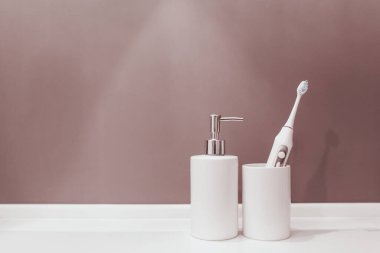 Beyaz seramik banyo aksesuarları sabun ve mor pastel arka planda izole edilmiş diş fırçası ile bir bardak.