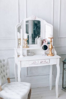 Güzel, beyaz bir iç mekan. Ahşap zemin aydınlatma duvarlı klasik oda pervazlı sandalye aynalı tuvalet masası, altın elementlerle süslenmiş.