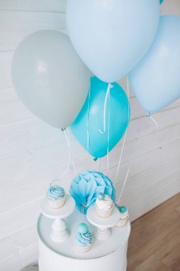 Renkli balonlar ve keklerle süslenmiş beyaz tahta bir duvar.