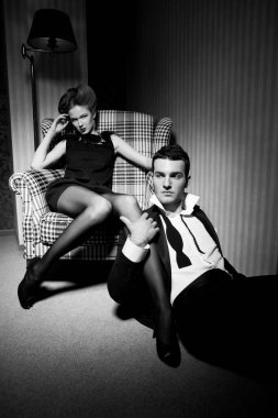 Odadaki gölgelerde klasik giysiler içinde tutkulu güzel bir çift: sandalyede oturan kadın, ayaklarının dibinde yatan bir adam.