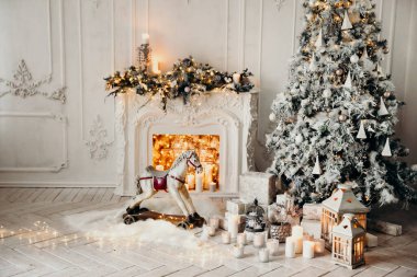 Beyaz bir odanın içinde Noel ağacı, süslü bir şömine, sallanan at ve yeni yıl hediyeleri olan bir oda.