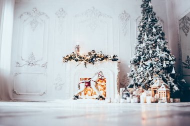 Beyaz bir odanın içinde Noel ağacı, süslü bir şömine, sallanan at ve yeni yıl hediyeleri olan bir oda.