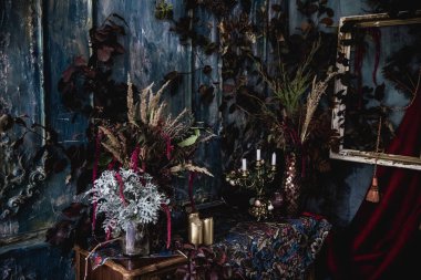 Kurumuş çiçekler, vazolar, avizeler, altın çerçeveli kumaşlar, lüks kraliyet tarzı ahşap bir masa, eski fenerlerle yanan mumlar.