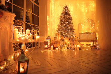 Noel iç tasarımında sıcak ve sıcak bir akşam, ışıklarla süslenmiş Xmas ağacı hediyeler, oyuncaklar, geyikler, mumlar, fenerler, kapalı alanda yanan çelenkler.