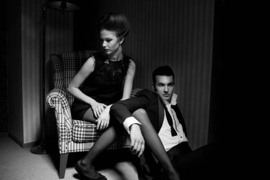 Odadaki gölgelerde klasik giysiler içinde tutkulu güzel bir çift: sandalyede oturan kadın, ayaklarının dibinde yatan bir adam.