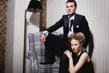 Odadaki gölgelerde klasik giysiler içinde tutkulu güzel bir çift: sandalyede oturan adam, ayaklarının dibinde yatan kadın.