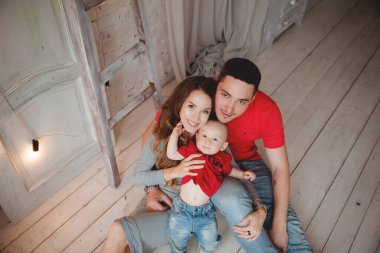 Mutlu ebeveynler, erkek bebekle odada poz veriyorlar.