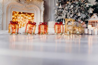 Kırmızı-turuncu oyuncak tren, beyaz zeminde ışıkları olan bir Noel ağacının arka planında ışıklar, çelenkler ve şöminesi olan.