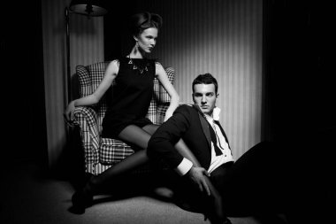 Odadaki gölgelerde klasik giysiler içinde tutkulu güzel bir çift: sandalyede oturan kadın, ayaklarının dibinde yatan bir adam.