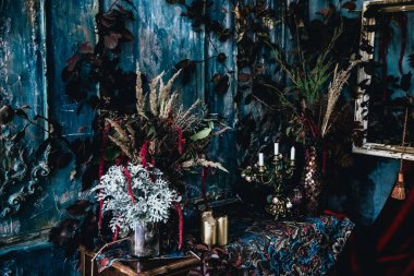 Kurumuş çiçekler, vazolar, avizeler, altın çerçeveli kumaşlar, lüks kraliyet tarzı ahşap bir masa, eski fenerlerle yanan mumlar.