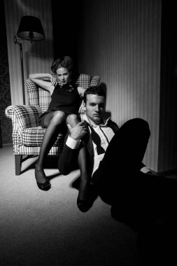 Odadaki gölgelerde klasik giysiler içinde tutkulu güzel bir çift: sandalyede oturan kadın, ayaklarının dibinde yatan bir adam.