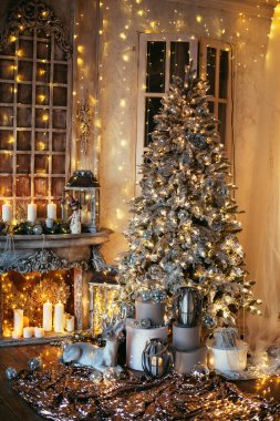 Noel iç tasarımında sıcak ve sıcak bir akşam, ışıklarla süslenmiş Xmas ağacı hediyeler, oyuncaklar, geyikler, mumlar, fenerler, kapalı alanda yanan çelenkler.