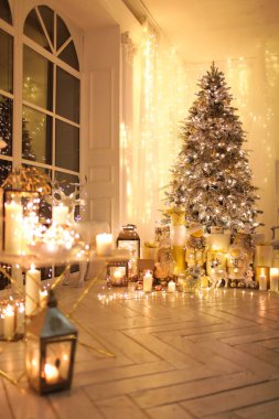 Noel iç tasarımında sıcak ve sıcak bir akşam, ışıklarla süslenmiş Xmas ağacı hediyeler, oyuncaklar, geyikler, mumlar, fenerler, kapalı alanda yanan çelenkler.