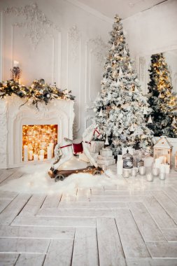 Beyaz bir odanın içinde Noel ağacı, süslü bir şömine, sallanan at ve yeni yıl hediyeleri olan bir oda.