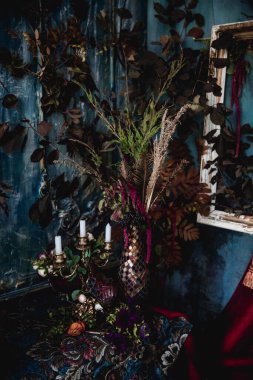 Kurumuş çiçekler, vazolar, avizeler, altın çerçeveli kumaşlar, lüks kraliyet tarzı ahşap bir masa, eski fenerlerle yanan mumlar.