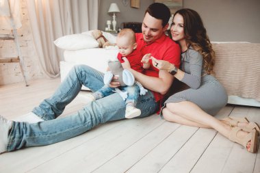 Mutlu ebeveynler, erkek bebekle odada poz veriyorlar.